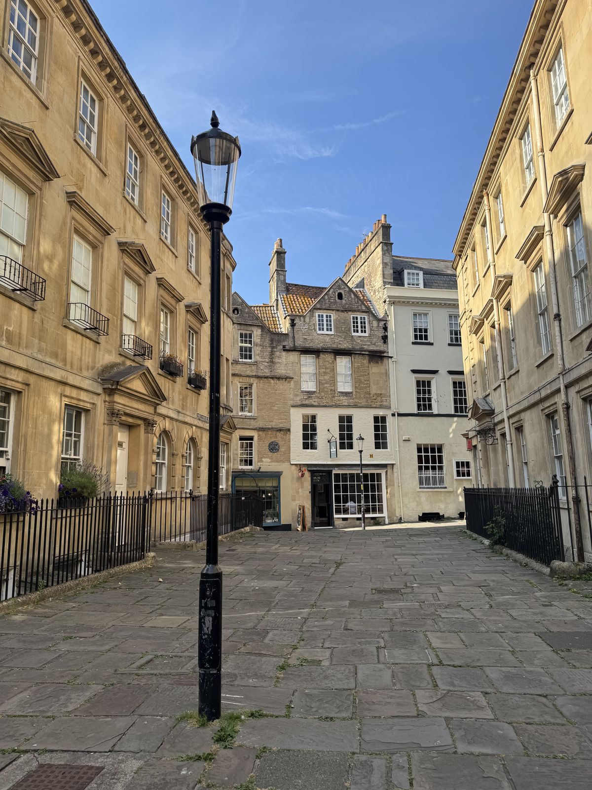 A quiet flagstone lane in Bath with a gas lamp and honey-coloured Bath stone terraces, away from the main sights